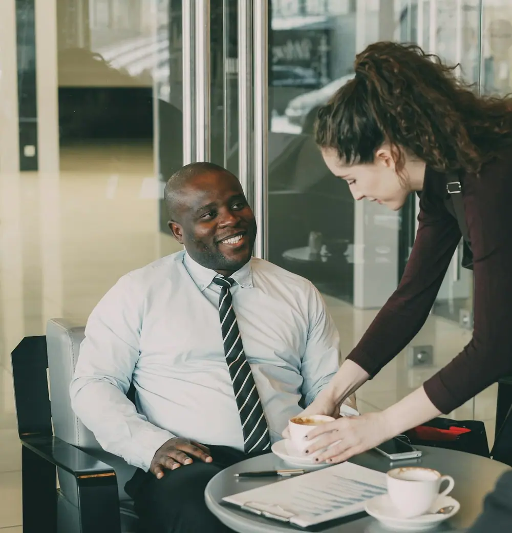A meeting around a table, a man in a tie smiling as a colleague talks