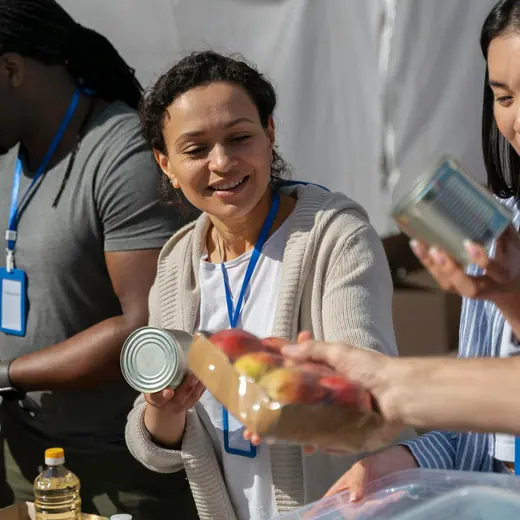 Volunteers with lanyards smiling as they pack food and cans into boxes