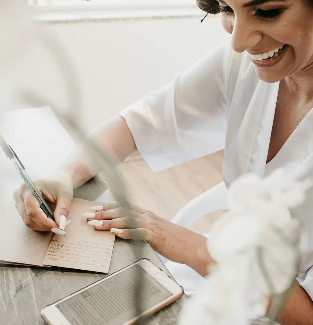A woman smiling as she writes a card at a bright desk